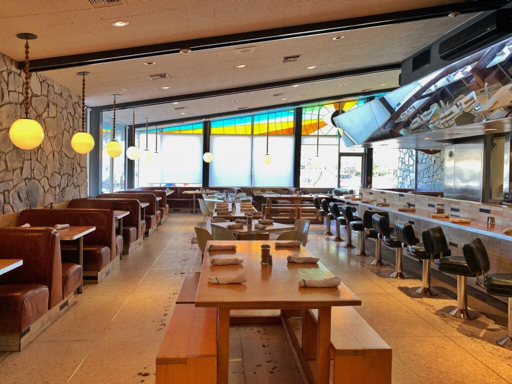 Retro-inspired Kings Highway restaurant at the Ace Hotel Palm Springs, featuring leather booths, globe pendant lights, stone walls, and colorful midcentury stained glass windows — a stylish diner for design lovers and foodies visiting the desert.