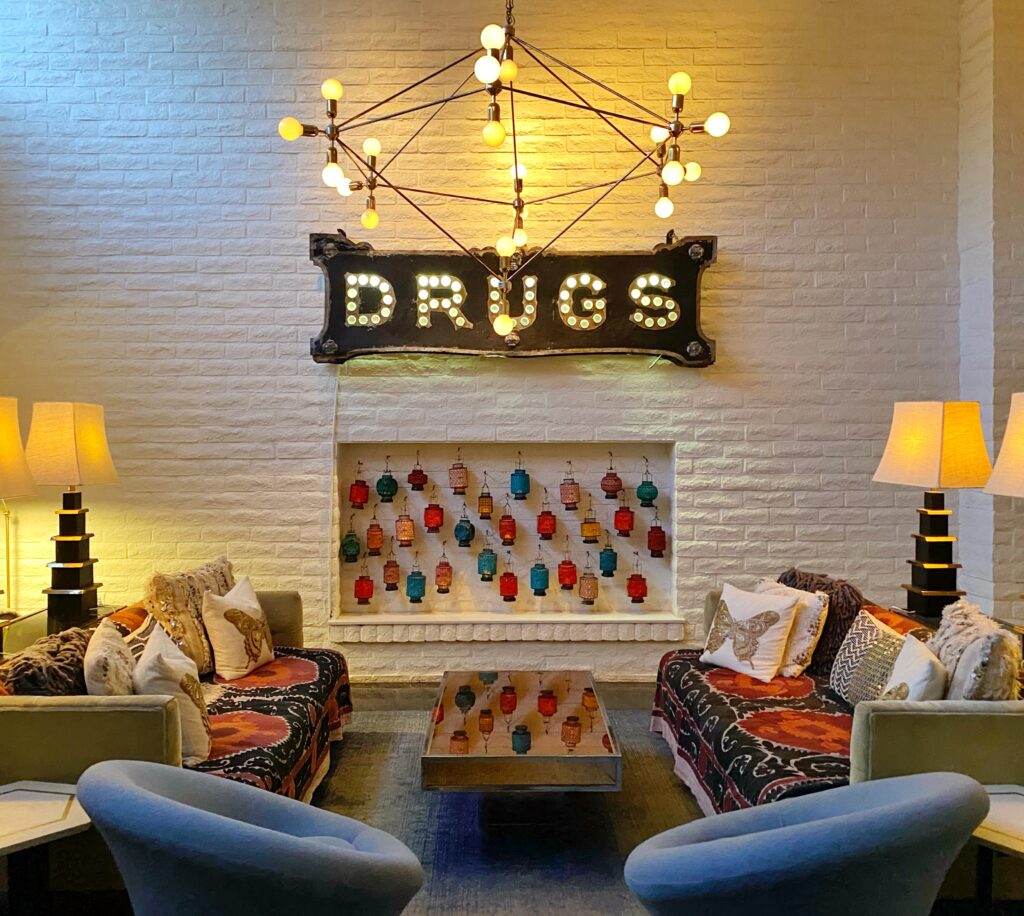 Eclectic lobby lounge at the Parker Palm Springs featuring the iconic illuminated ‘Drugs’ sign, colorful hanging lanterns, patterned sofas, and midcentury-inspired lighting.