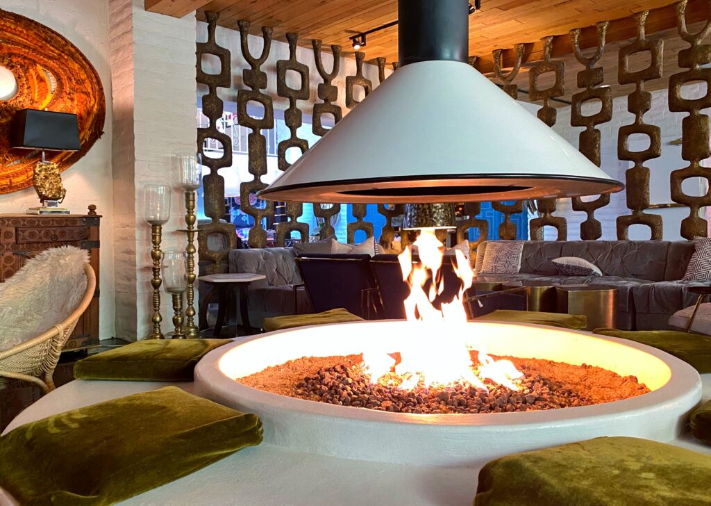 Mid-century modern lounge at the Parker Palm Springs featuring a central fire pit, sculptural room divider, velvet cushions, and warm ambient lighting.