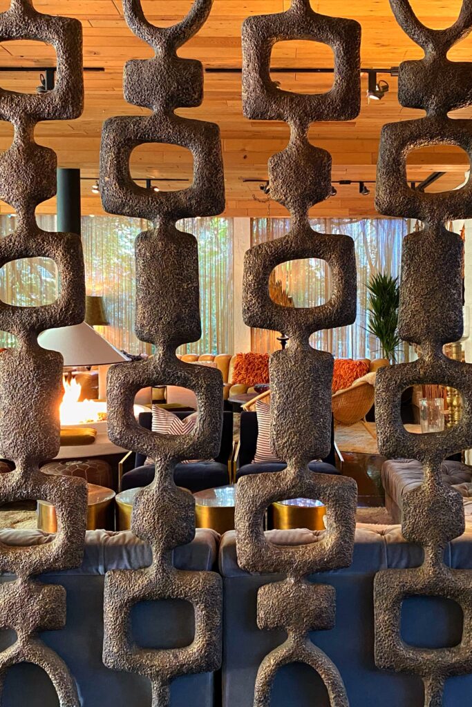 Midcentury modern textured room divider screen wall at the Parker Palm Springs, with a cozy lounge, fire pit, and stylish vintage seating visible through the geometric cutouts.