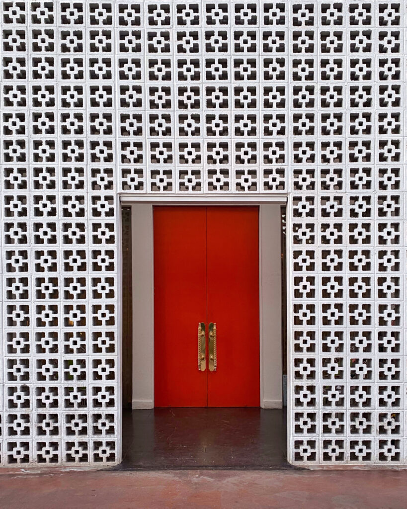 Iconic bright orange door at the Parker Palm Springs framed by a white mid-century modern breeze block wall with geometric patterns.