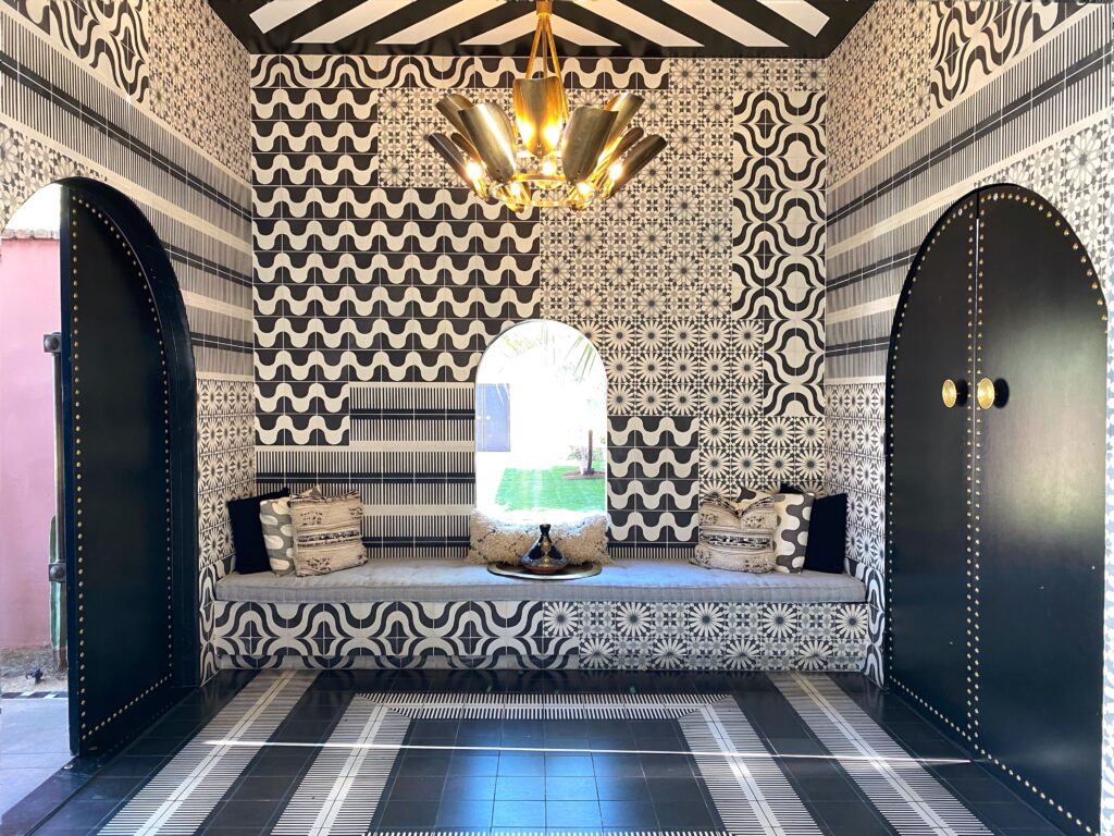 Maximalist pattern-rich lounge interior at The Sands Hotel in Indian Wells, featuring black-and-white Moroccan-inspired tile walls, striped ceiling, built-in bench seating with textured pillows, and dramatic black arched doors — a bold, design-forward Palm Springs boutique-hotel space.