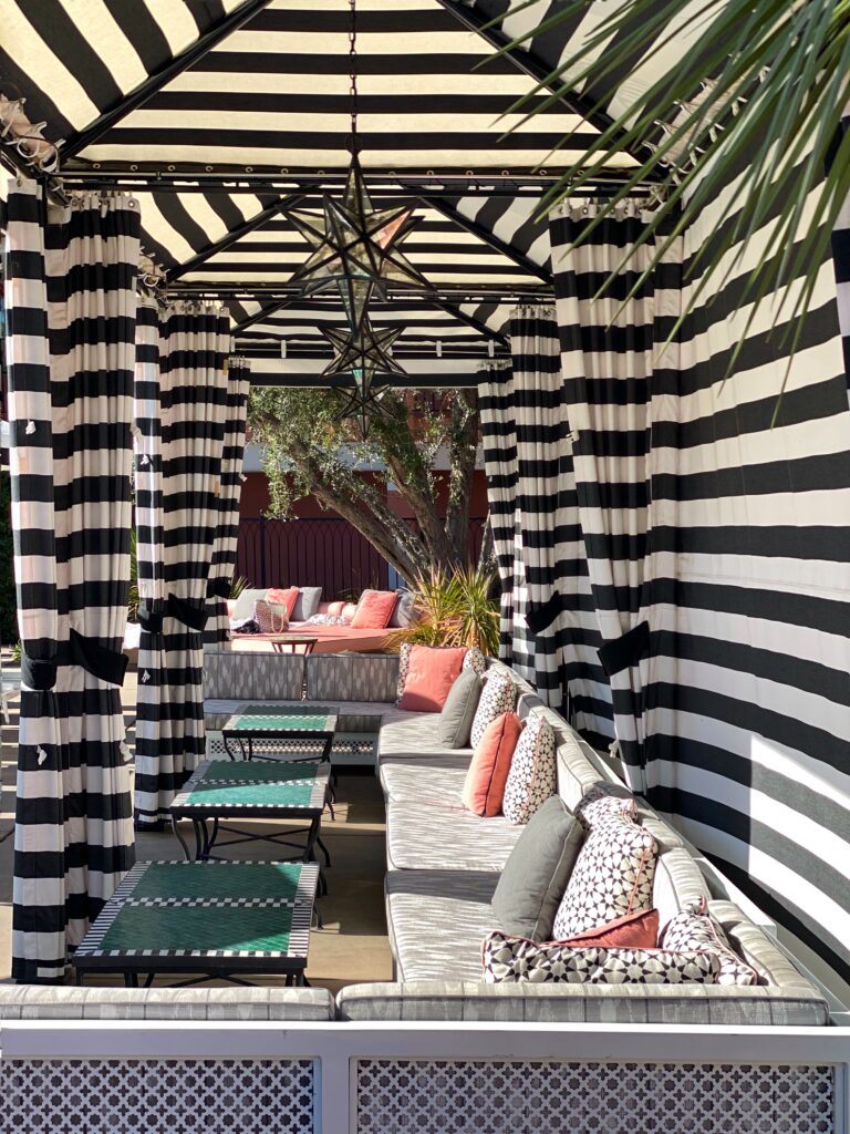 Black-and-white striped cabana at The Sands Hotel in Indian Wells featuring star-shaped pendant lanterns, cushioned lounge seating with patterned pillows, and green mosaic-topped tables in a chic Moroccan-inspired poolside setting.