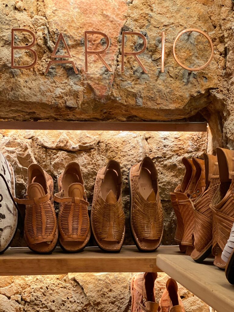 Handwoven leather huarache sandals displayed beneath the Barrió sign inside Tetetlán in Mexico City, set against a textured volcanic stone wall; the warm leather tones, artisanal craftsmanship, and architectural backdrop reflect Tetetlán’s design-forward approach to Mexican tradition, hospitality, and curated travel retail.