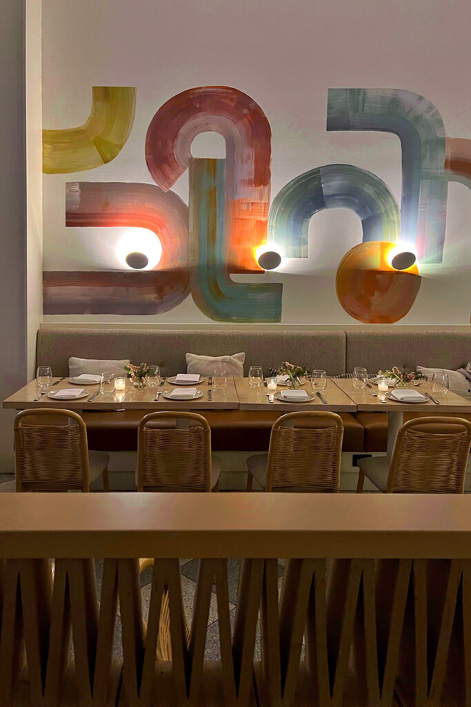Il Fiorista dining room in New York City featuring abstract painted wall art, woven rattan chairs, candlelit tables, and a warm modern aesthetic—an art-forward restaurant interior in Manhattan’s NoLita neighborhood.