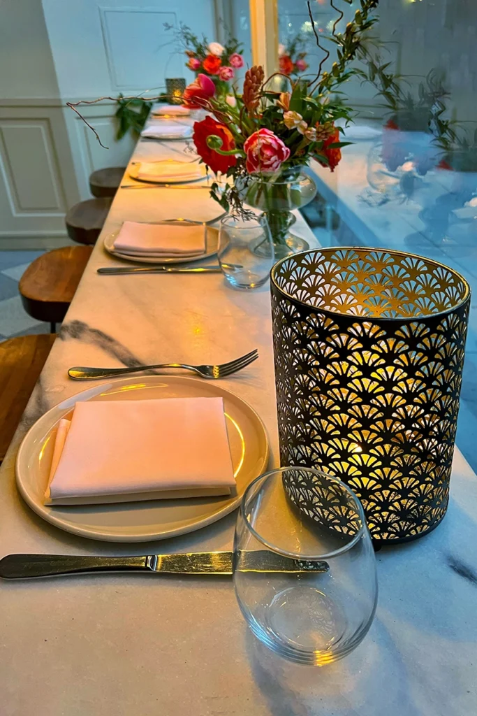 Candlelit marble communal table at Il Fiorista in NoLIta, New York City, styled with blush linen napkins, brass cutlery, floral centerpieces, and warm ambient lighting—an intimate, design-forward dining experience.