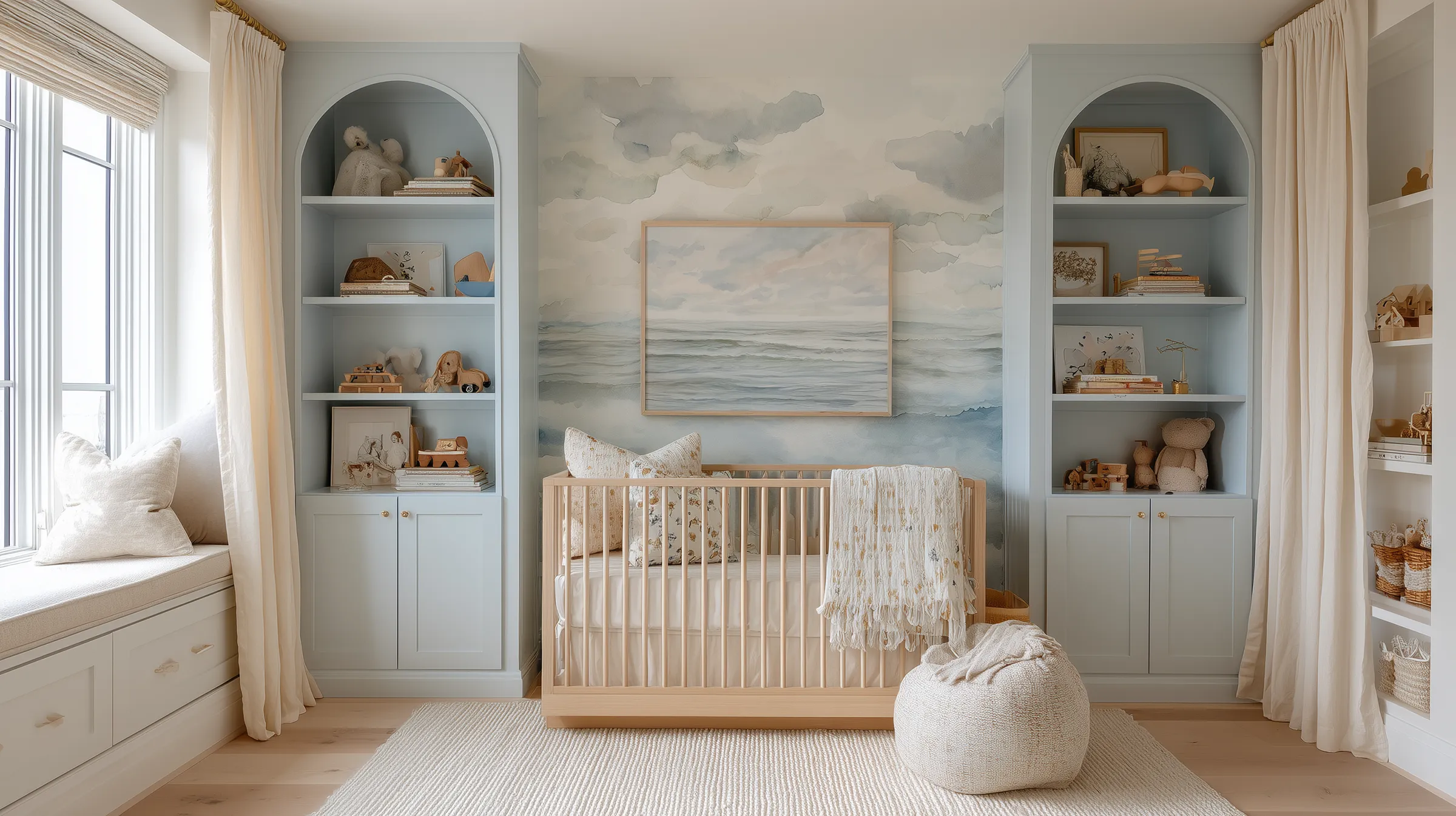 Coastal nautical nursery with a watercolor ocean mural, light wood crib, and built-in blue cabinetry, featuring soft neutral textiles, natural wood toys, and serene seaside colors for a calm, timeless baby room design