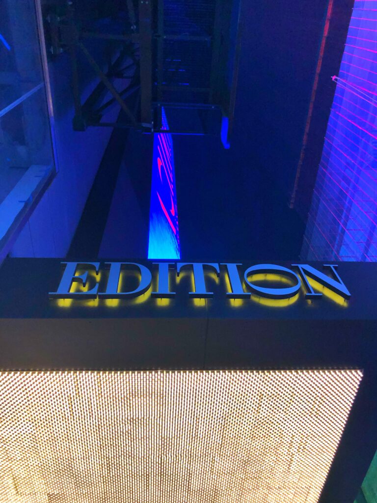 Neon-lit Edition Hotel sign in Times Square, New York City, with moody blue and purple lighting and a sleek modern entrance design that appeals to travelers searching for aesthetic NYC hotels.