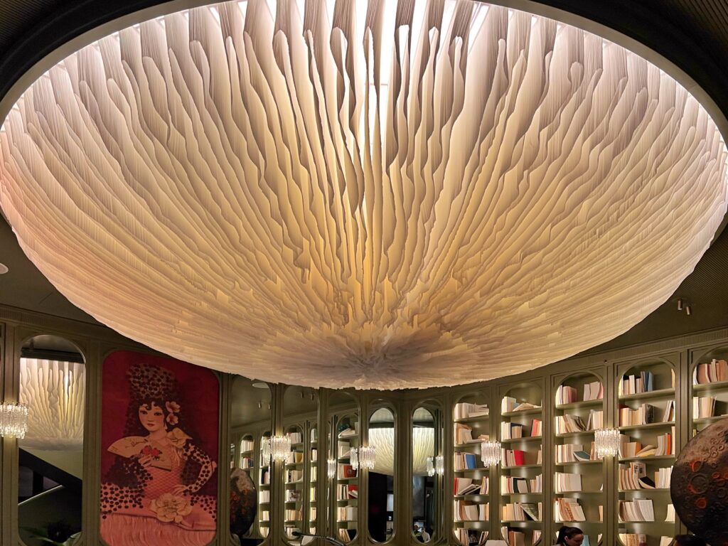 Randall Zieber chandelier in the lobby lounge at The Ritz-Carlton New York, NoMad, suspended above sage-green bookcases, mirrored arches, and the richly layered interiors designed by Lázaro Rosa-Violán Studio.