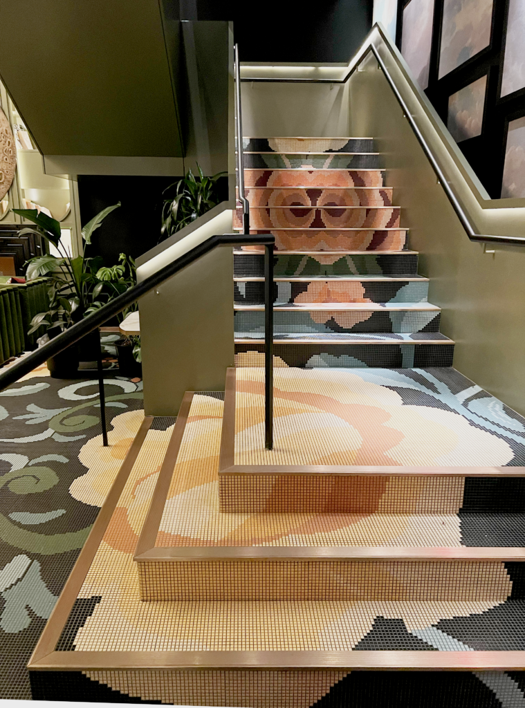 Mosaic staircase at The Ritz-Carlton New York, NoMad with oversized floral motifs, soft sage and blush tones, integrated stair lighting, and a biophilic, bloomcore-inspired interior design.