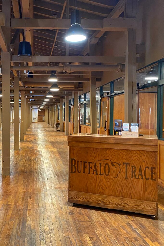 Buffalo Trace Distillery tour tasting room in Frankfort, Kentucky with an oak Buffalo Trace podium, vintage wood floors, factory lights, and long industrial hallway—classic Kentucky Bourbon Trail stop.