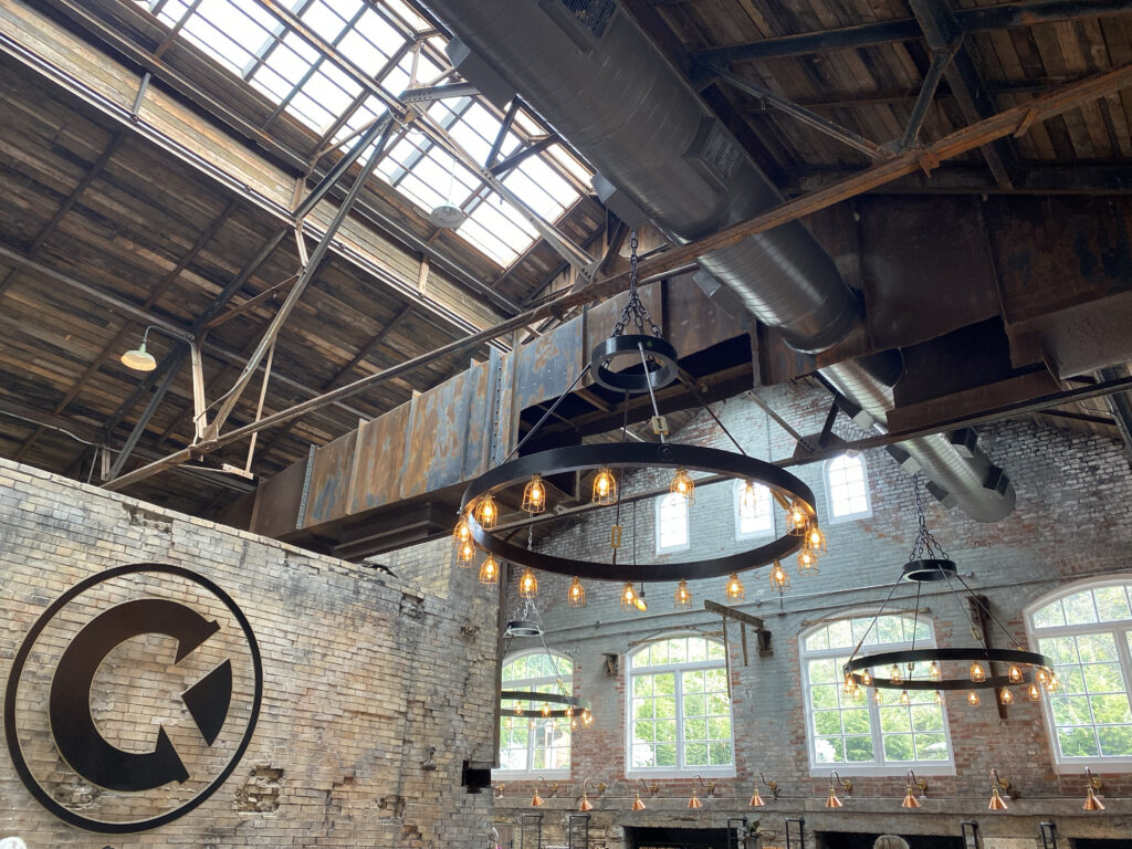 Castle & Key Distillery in Frankfort, Kentucky with exposed brick walls, skylights, tall factory windows, and large circular chandeliers—an aesthetic stop on the Kentucky Bourbon Trail.