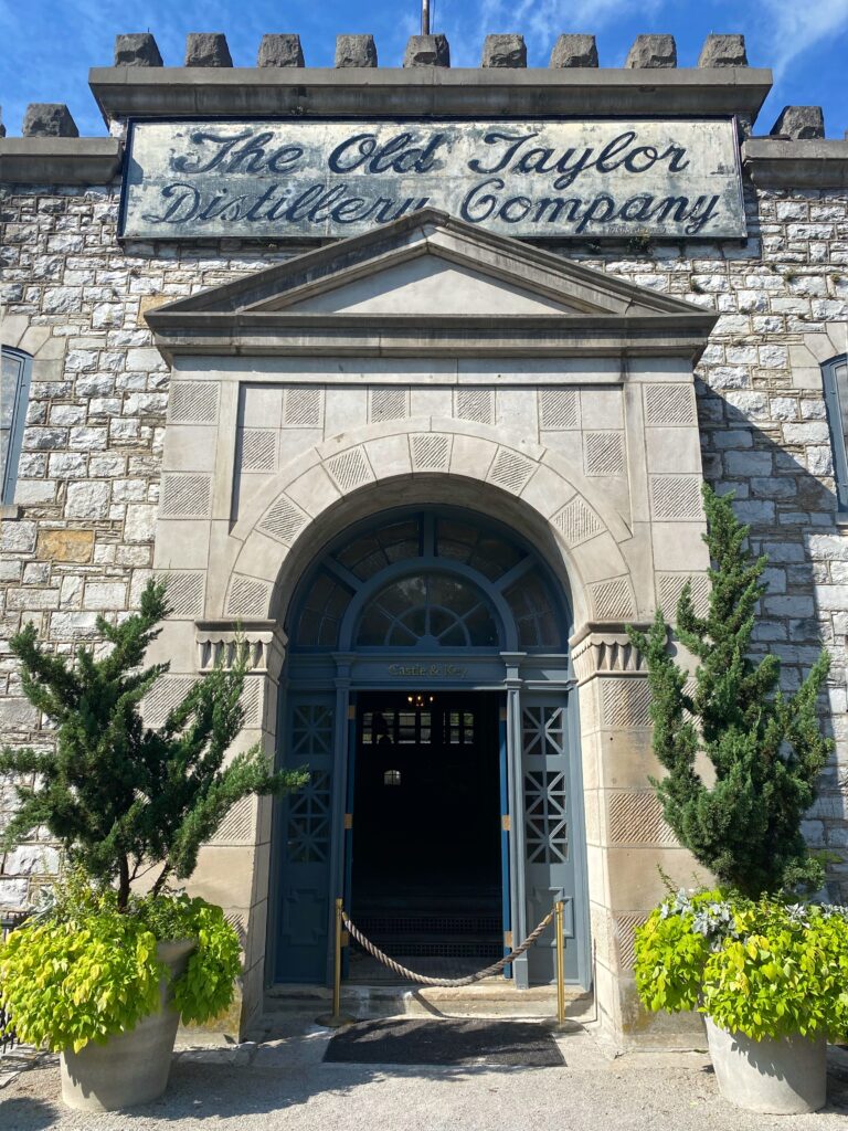 Entrance to Castle & Key Distillery at the historic Old Taylor Distillery in Frankfort, Kentucky, with a stone facade, arched doorway, and “The Old Taylor Distillery Company” sign—an iconic stop on the Kentucky Bourbon Trail.