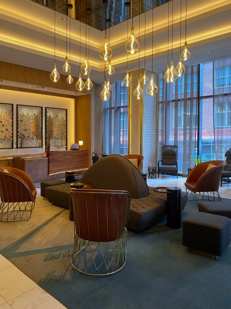Hotel Distil lobby in Louisville, Kentucky featuring sculptural lounge seating, warm amber pendant lights, and floor-to-ceiling windows overlooking Whiskey Row—an aesthetic hotel lobby near the Bourbon District.