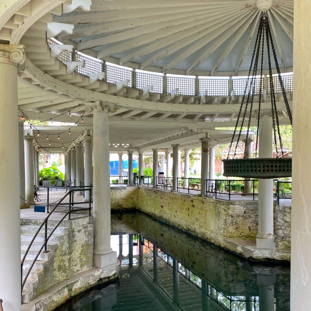 Historic springhouse at the Castle and Key Distillery on the Kentucky Bourbon Trail with a circular white colonnade, wooden roof beams, string lights, and a long reflection pool beneath the covered walkway—an aesthetic distillery stop in Kentucky.