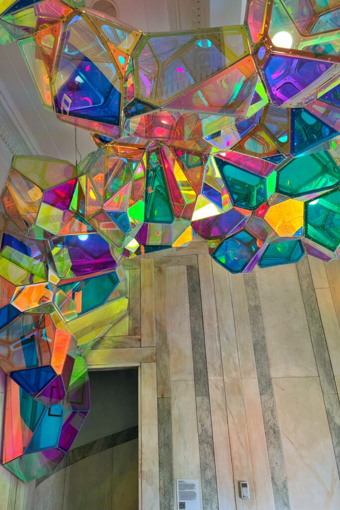 Spectralline, a rainbow acrylic art installation, wraps around the entrance inside 21c Museum Hotel Lexington in downtown Lexington, Kentucky. The vibrant geometric panels create a striking contrast against the renovated historic McKim, Mead & White building interior.