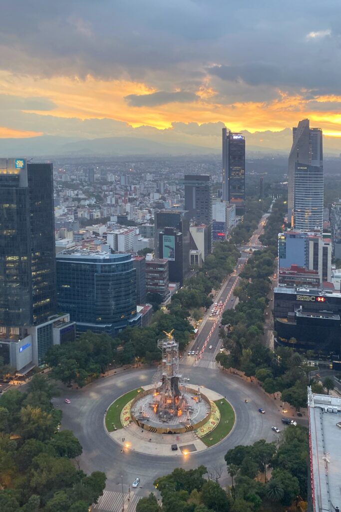Sunset view from Cityzen Rooftop Bar in Mexico City overlooking Ángel de la Independencia, Paseo de la Reforma, and the surrounding skyline. The golden sky, evening traffic, and high-rise buildings create a dramatic rooftop perspective of one of Mexico City’s most iconic avenues.