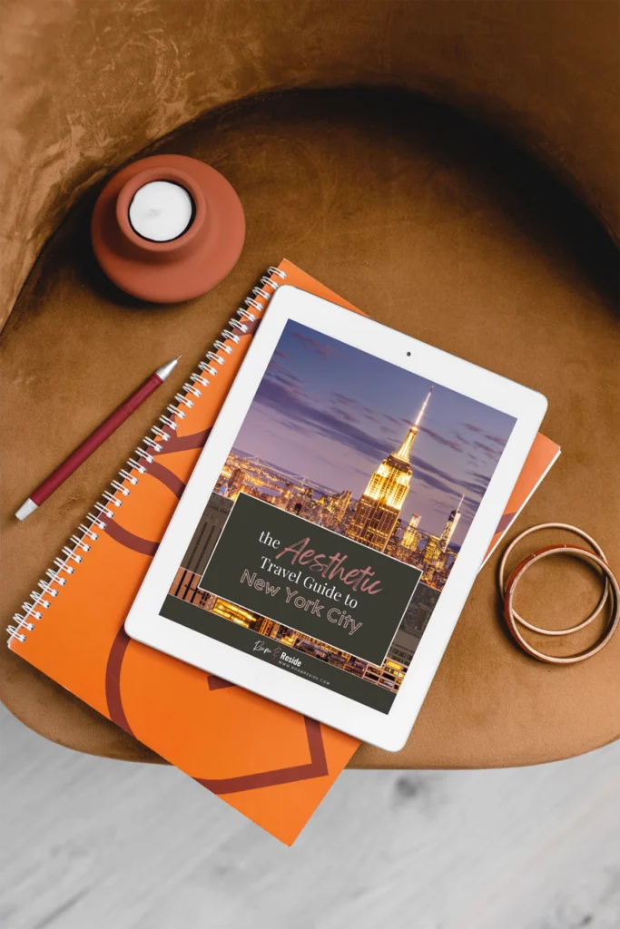 The Roam & Reside Aesthetic Travel Guide to New York City on an iPad, sitting in a leather chair with a spiral notebook.
