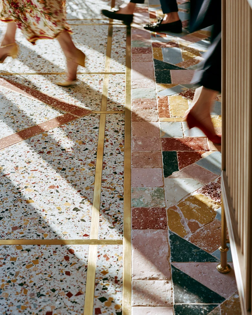 Close-up of people walking across a colorful patterned tile floor with brass inlay, terrazzo, and warm sunlight casting shadows across the surface. This image captures an aesthetic living moment focused on noticing beauty in everyday details like color, texture, movement, and light.